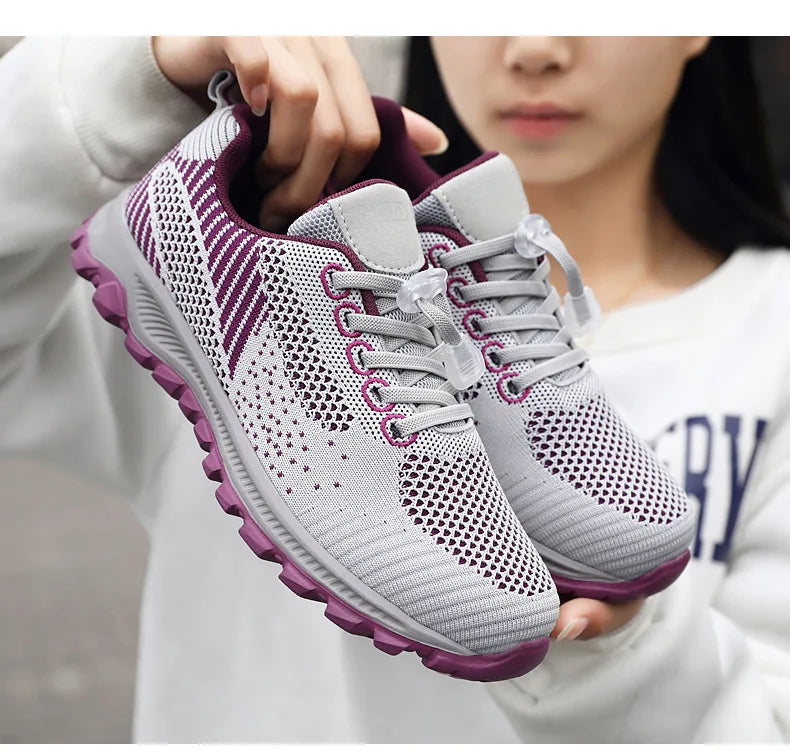 Woman holds up a pair of lightweight, breathable gray and purple athletic walking shoes with toggle laces.
