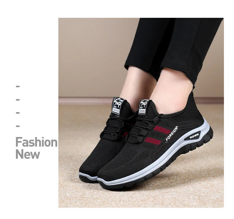 A person models stylish black mesh sneakers with red stripes and white soles, showcasing a comfortable and trendy shoe option.
