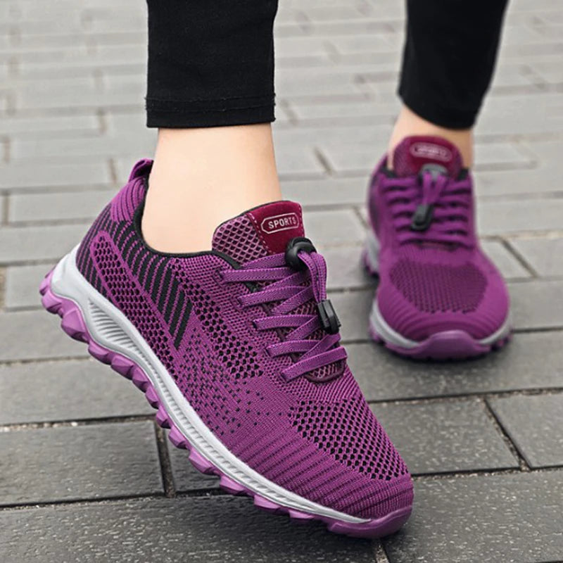 A person wears purple mesh walking shoes on a paved surface.
