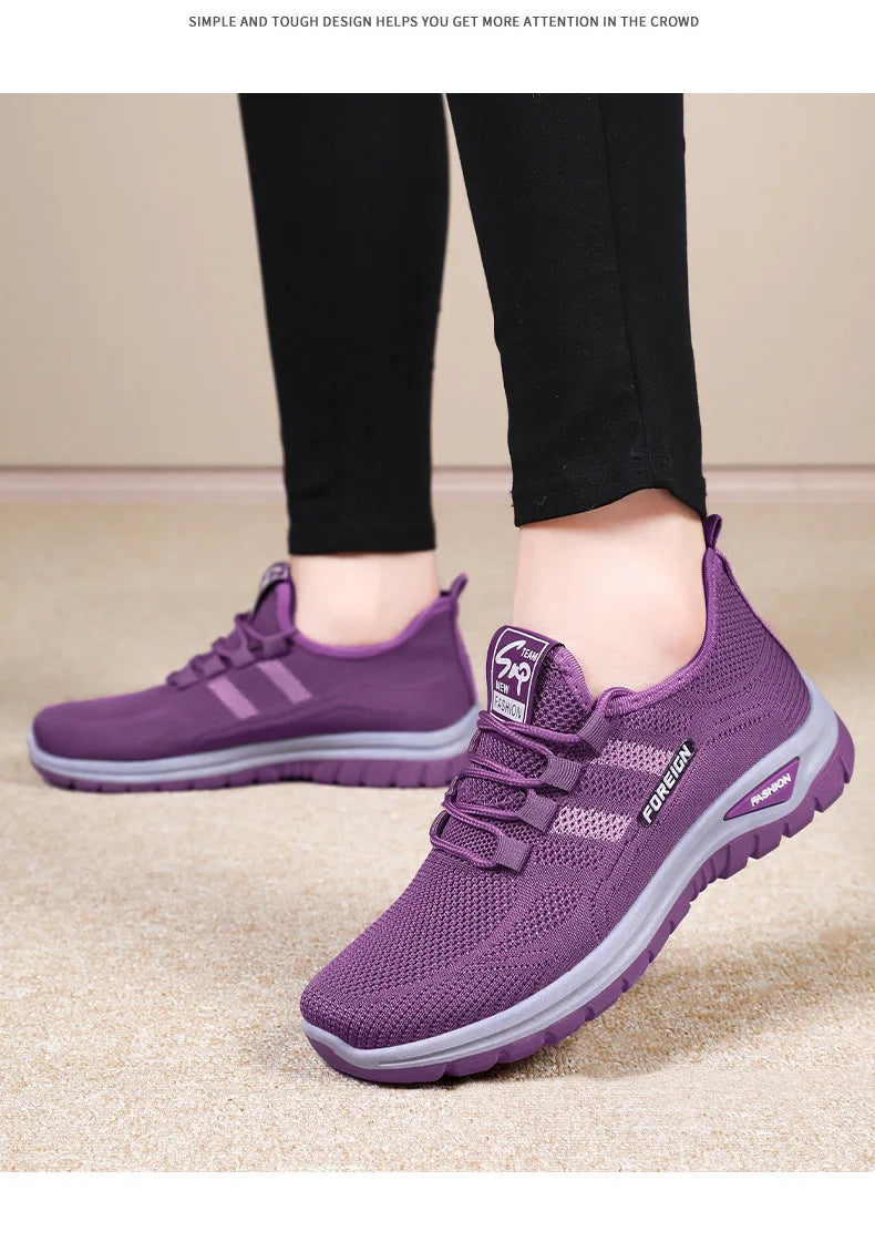 A person models comfortable purple mesh sneakers with gray soles.
