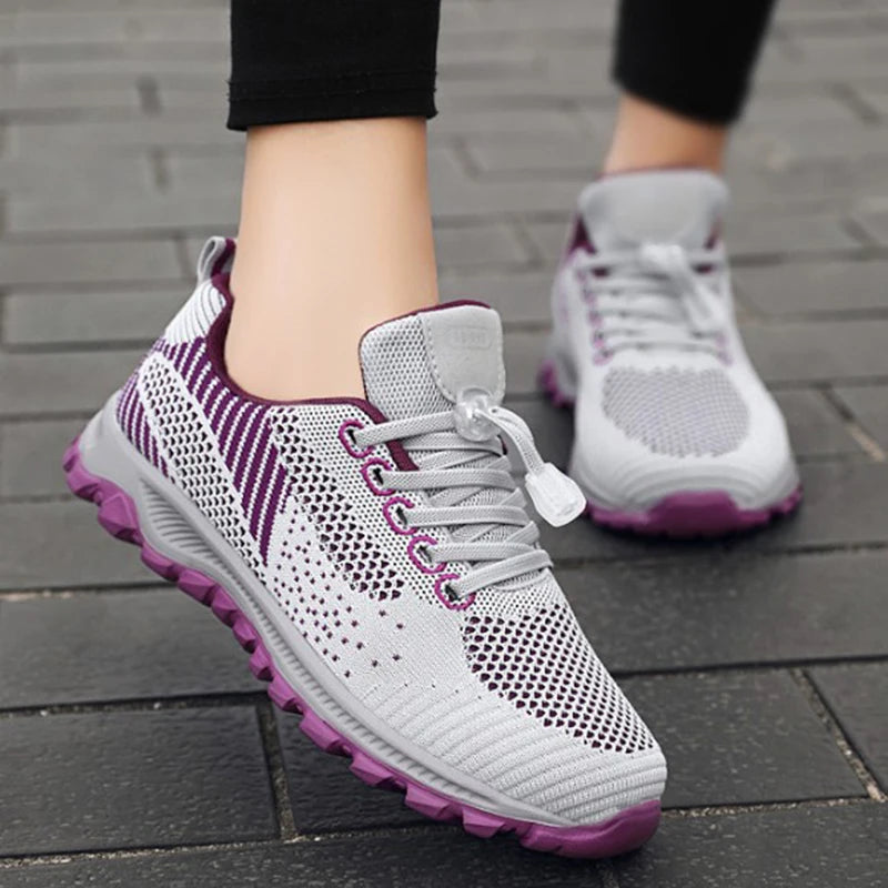 Person wears white and purple athletic sneakers on a brick path.
