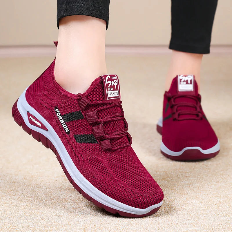 A person models maroon knit running shoes with a white stripe detail on a beige carpet.
