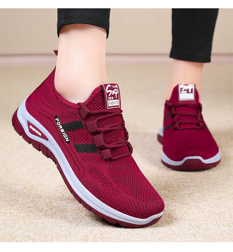 A person models maroon knit athletic shoes with white soles and decorative laces.
