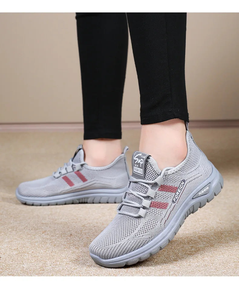 A person wears comfortable gray athletic running shoes with a red stripe while standing.
