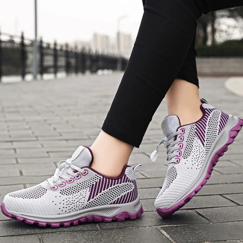 Person wears gray and purple athletic walking shoes on a city sidewalk.
