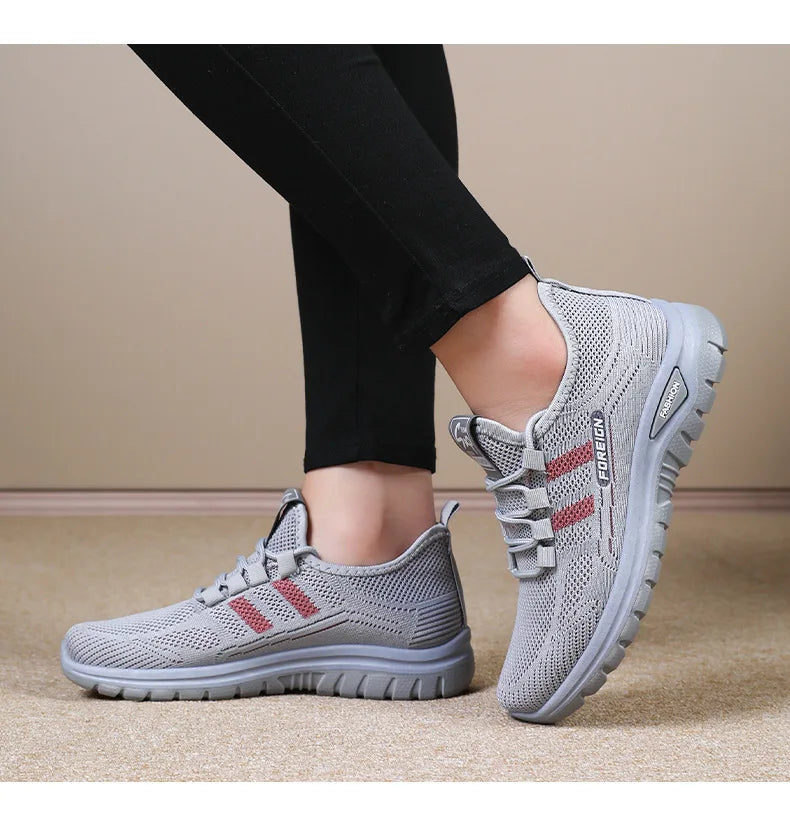 A person models gray mesh running shoes with red stripes and "FOREIGN" and "FASHION" labels.
